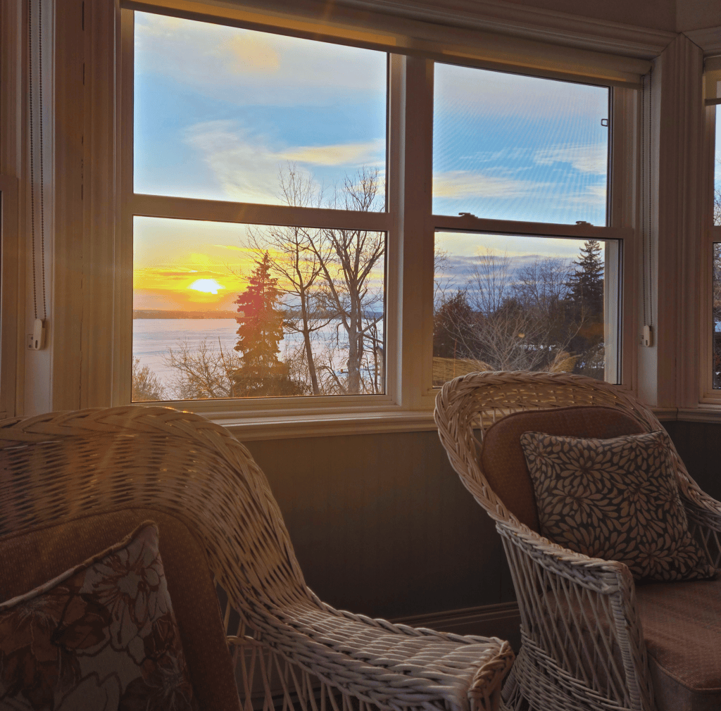 The sitting room at Loretto Maryholme Retreat centre, wicker chairs and window showing the lake and sunset at dusk